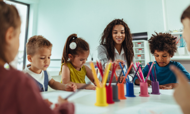 Child care provider sitting at a craft table with 5 kids using coloured pencils.