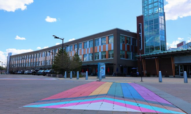 Close-up of the County's pride crosswalk with the progress flag design, with the Community Centre building in the background.