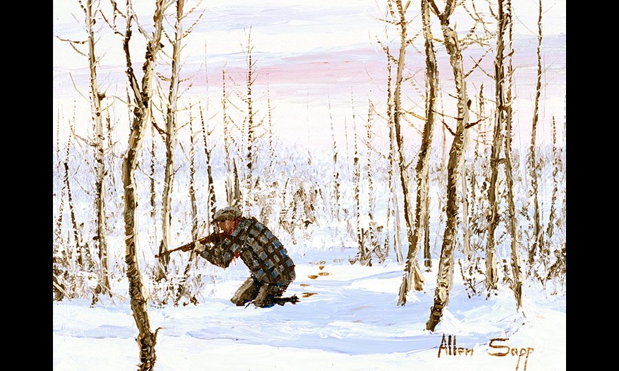 Man with a hunting rifle kneels in the snow in the woods.