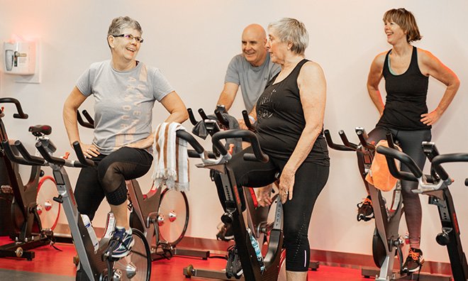 Adult wellness spin class with smiling participants.