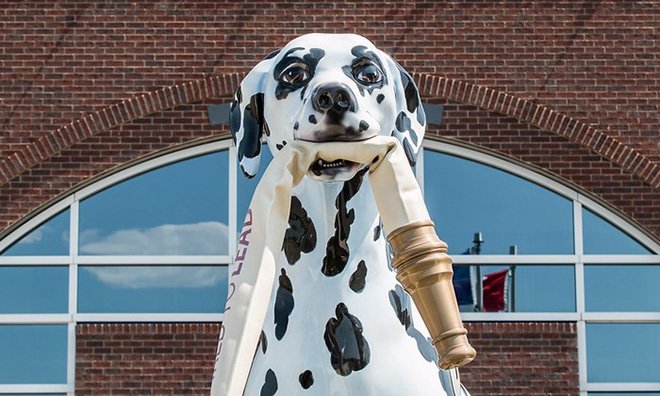 Close up of a large sculpture of a dalmatian dog holding the end of a fire hose in its mouth.