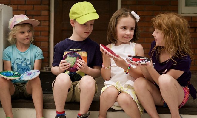Four children are sitting outside on a step showing each other the visual art they created