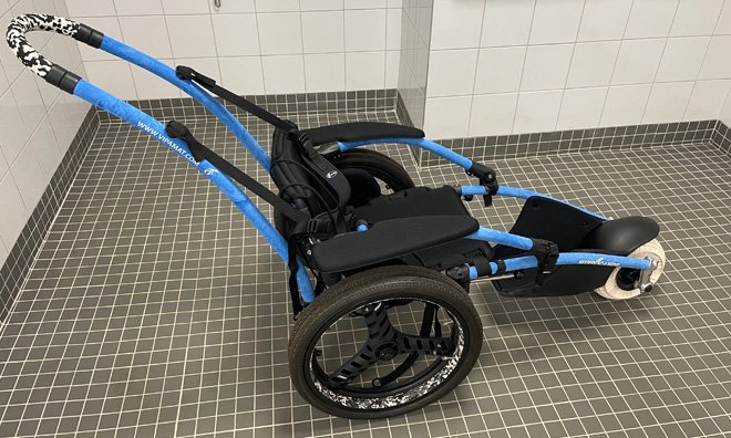 An elongated black and blue wheelchair with two side wheels and a larger, rounded front wheel in the shape of a ball.