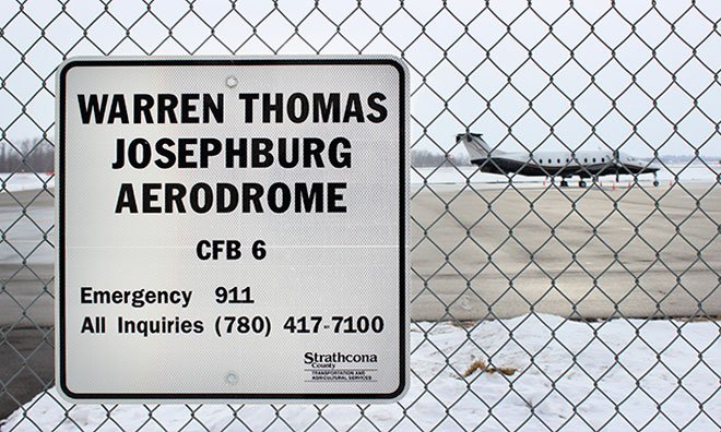Image of sign on fence that says Josephburg Aerodrome with a plane in the background