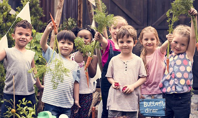 Image of school age children in a garden holding up vegetables