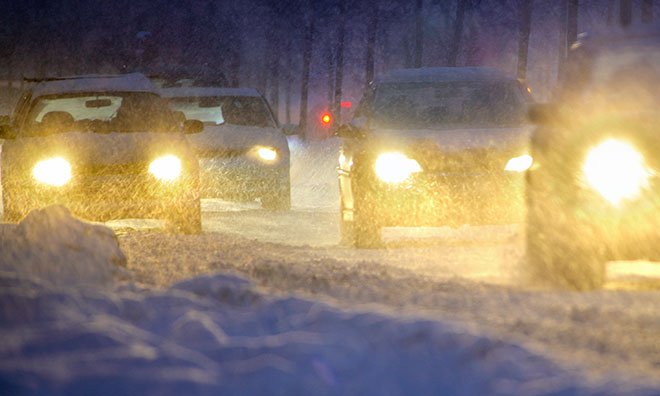 Image of cars driving at night during the winter with their headlights on