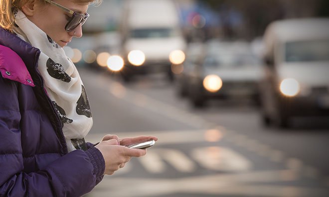 Image of pedestrian texting with cars in the background