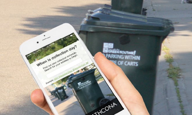 Image of a hand holding a phone in front of a black garbage cart. The screen of the phone has text that says 'when is collection day?'