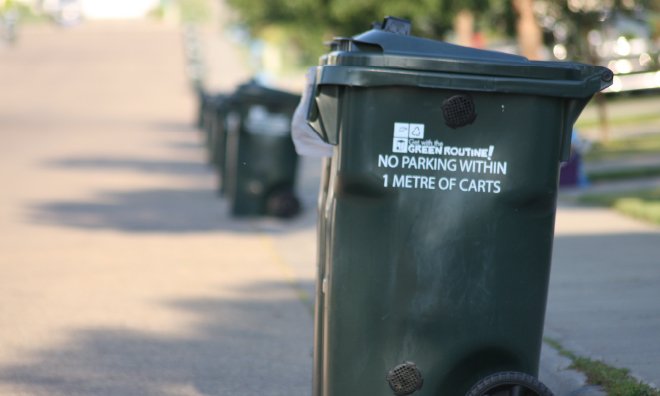 Image of dark green organics carts lined up along the curb on a residential street.