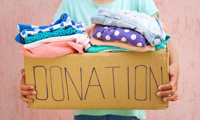 Woman holding a box of clothes with the word donation written on it.