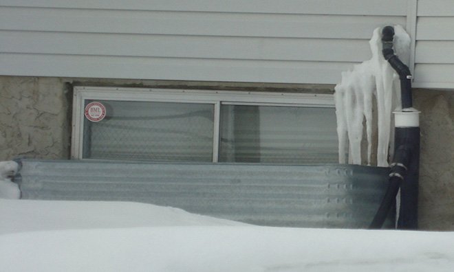 Image of a sump pump discharge pipe with long icicles built up under it.