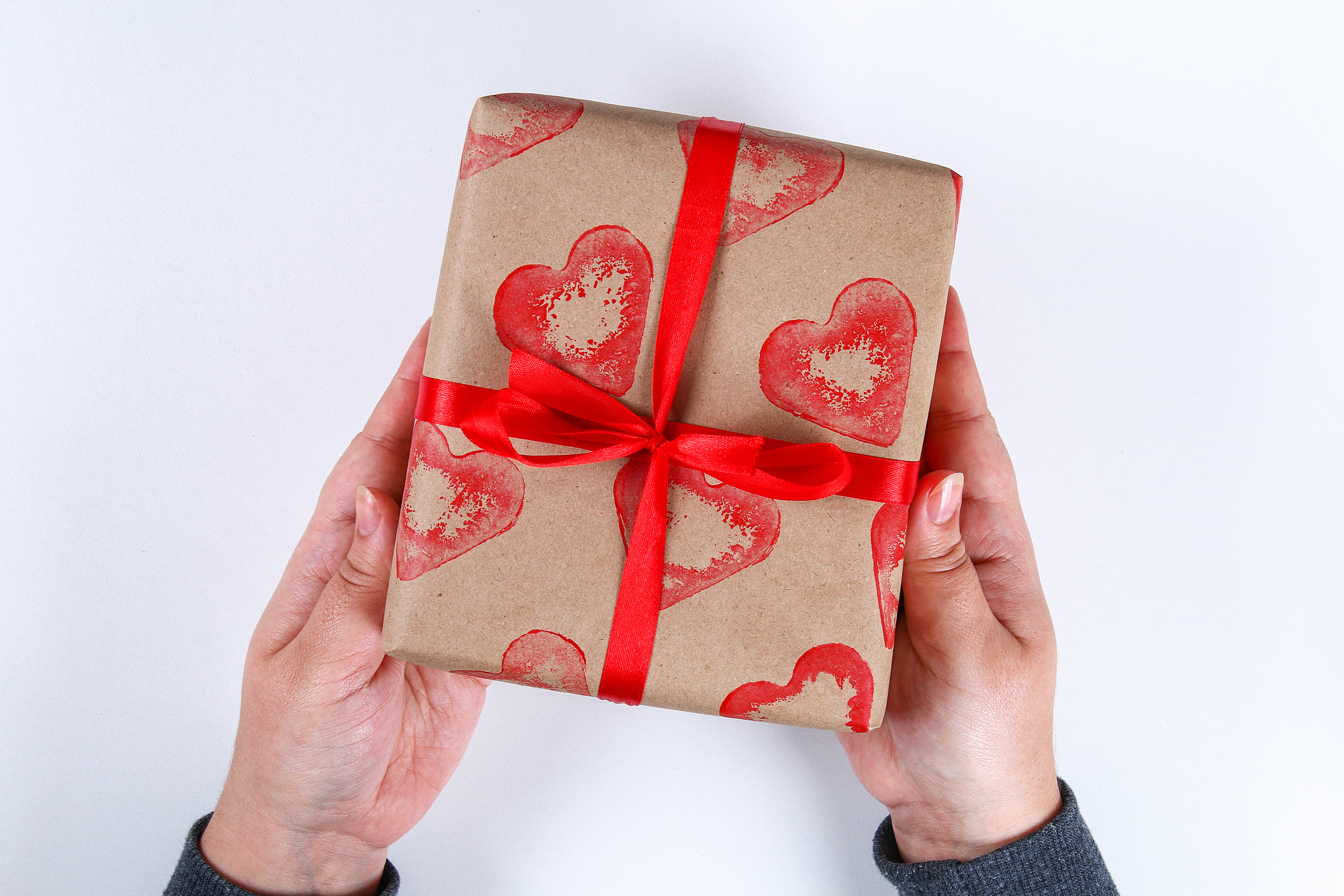 two hands holding a christmas gift with a red ribbon