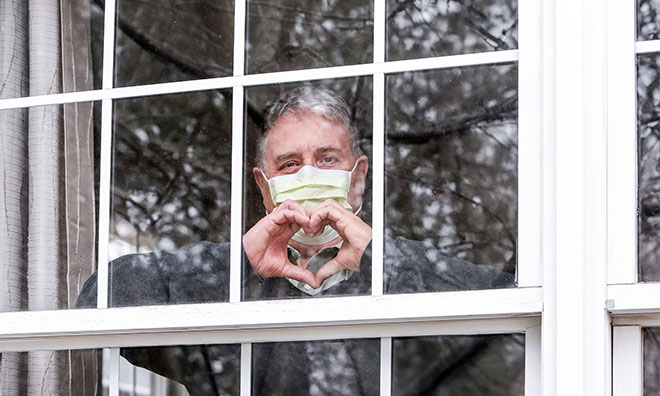 Middle age man behind a window, making a heart shape with his hands