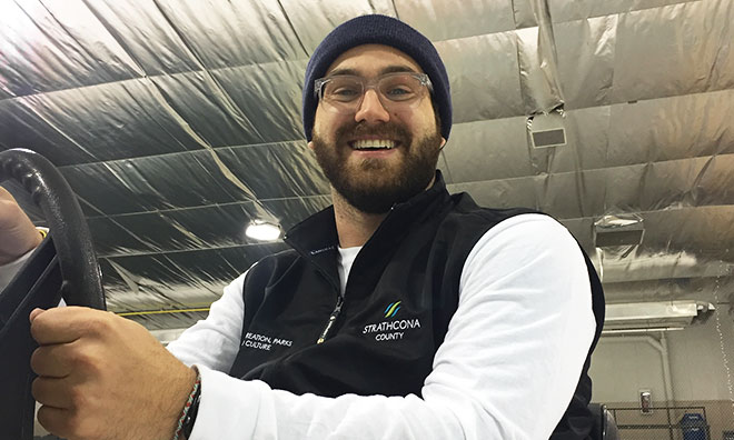Strathcona County employee smiles at the camera while operating a zamboni