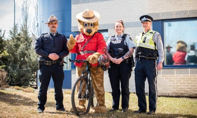 Safety bear riding its bike, posing for a picture with officers