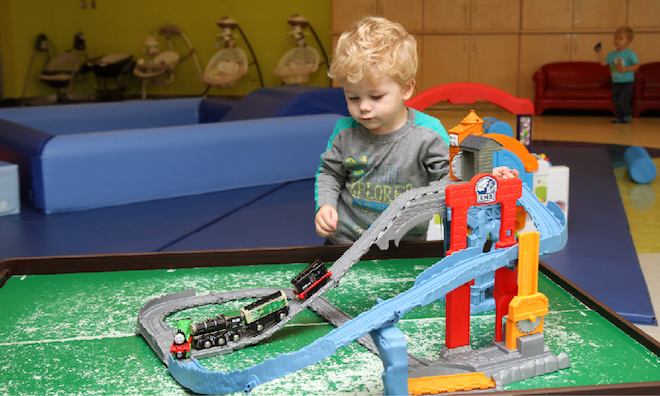 Young blonde boy playing with a car set on a green table.