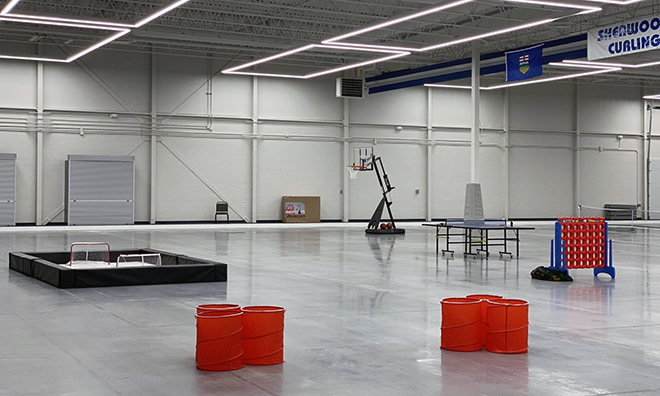 large dry surface area with cement flooring and red playing blocks. A basketball hoop appears in the background.