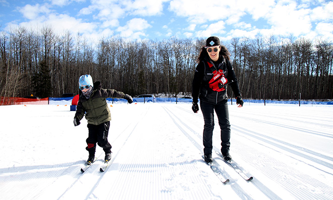 Cross-country skiing lesson with instructor and student on side by side tracks.