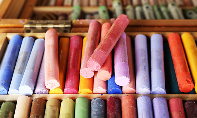 Various colourful pastels are shown next to each other in a wooden case