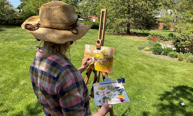 Woman with large hat painting on a small easel outdoors on a sunny day