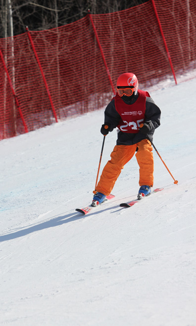 Skiier wearing orange ski pants, a black jacket and red helmet carving on a downhill slope.