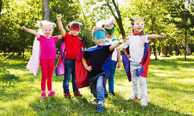 Group of young children dressed up in various superhero costume, holding each others' hands