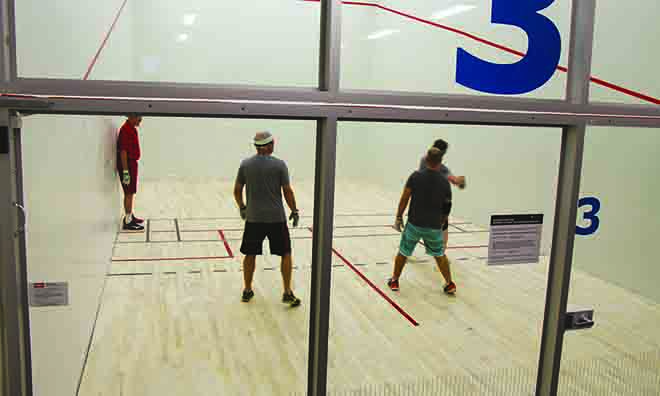 Three men are shown playing squash on an enclosed court that features a movable wall