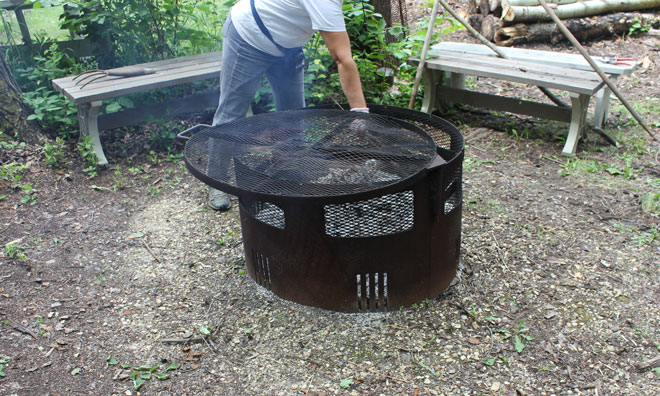 Person covering a firepit with a metal cover