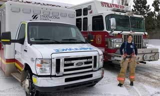Female firefighter/paramedic in front of ambulance and fire truck