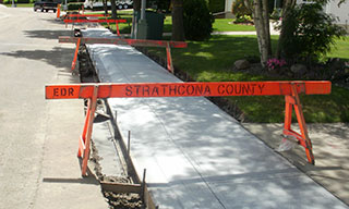 Newly poured concrete sidewalk blocked by construction signs.