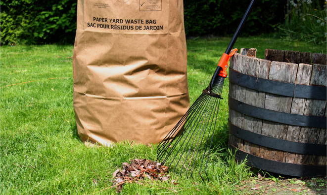 A paper yard waste bag with a pile of leaves in front of it and a rake.