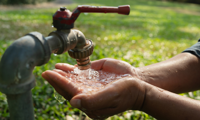 Image of a water tap in a field with water running into cupped hands below.