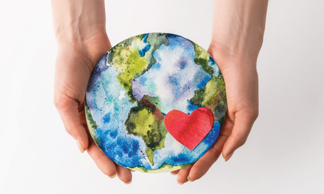 Image of hands holding a paper cut out of the earth with a heart on it.