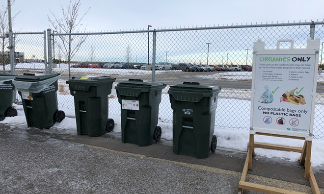 Image of green organics carts against a chainlink fence.