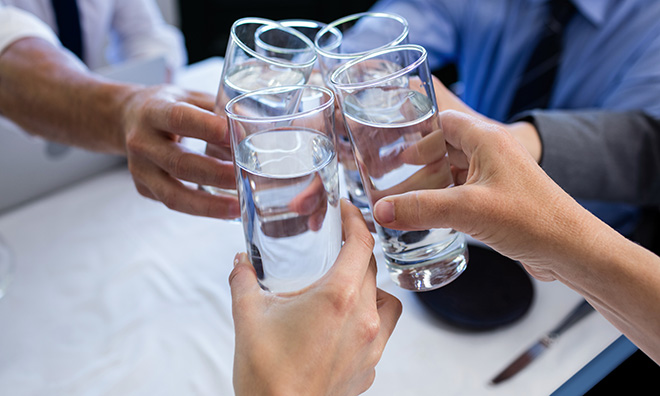 Image of four people tapping their glasses of water together.