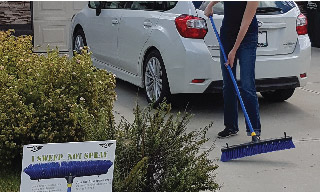 Image of a woman sweeping her driveway with a blue broom.