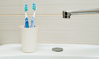 Image of a bathroom sink with two toothbrushes in a cup.