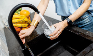 Image of a woman filling a glass of water from the kitchen tap.