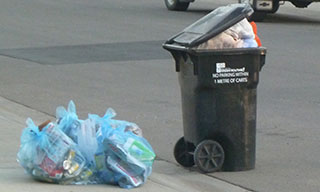 Image of waste cart full of garbage bags so that the lid cannot close.