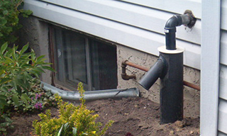 Image of the side of a house showing a window well, beside it is the sump pump discharge pipe.