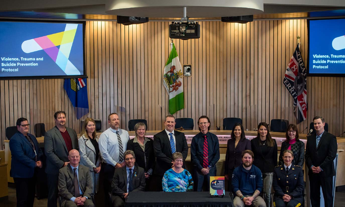 Group photo of 16 leaders from community organizations in Council Chambers posing with VTSP Protocol document before signing